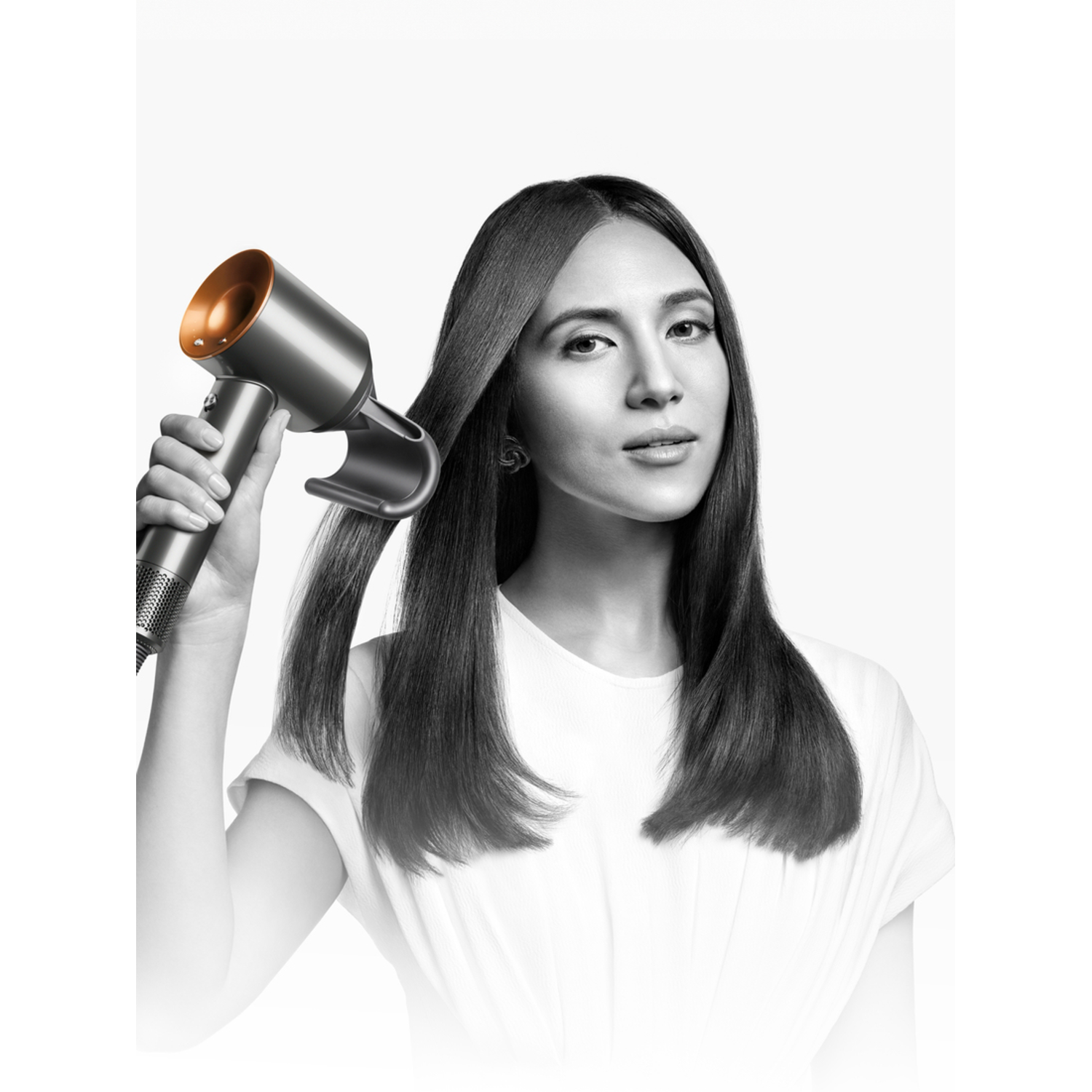 Woman styling her long, dark hair with a silver and copper Dyson hair dryer.