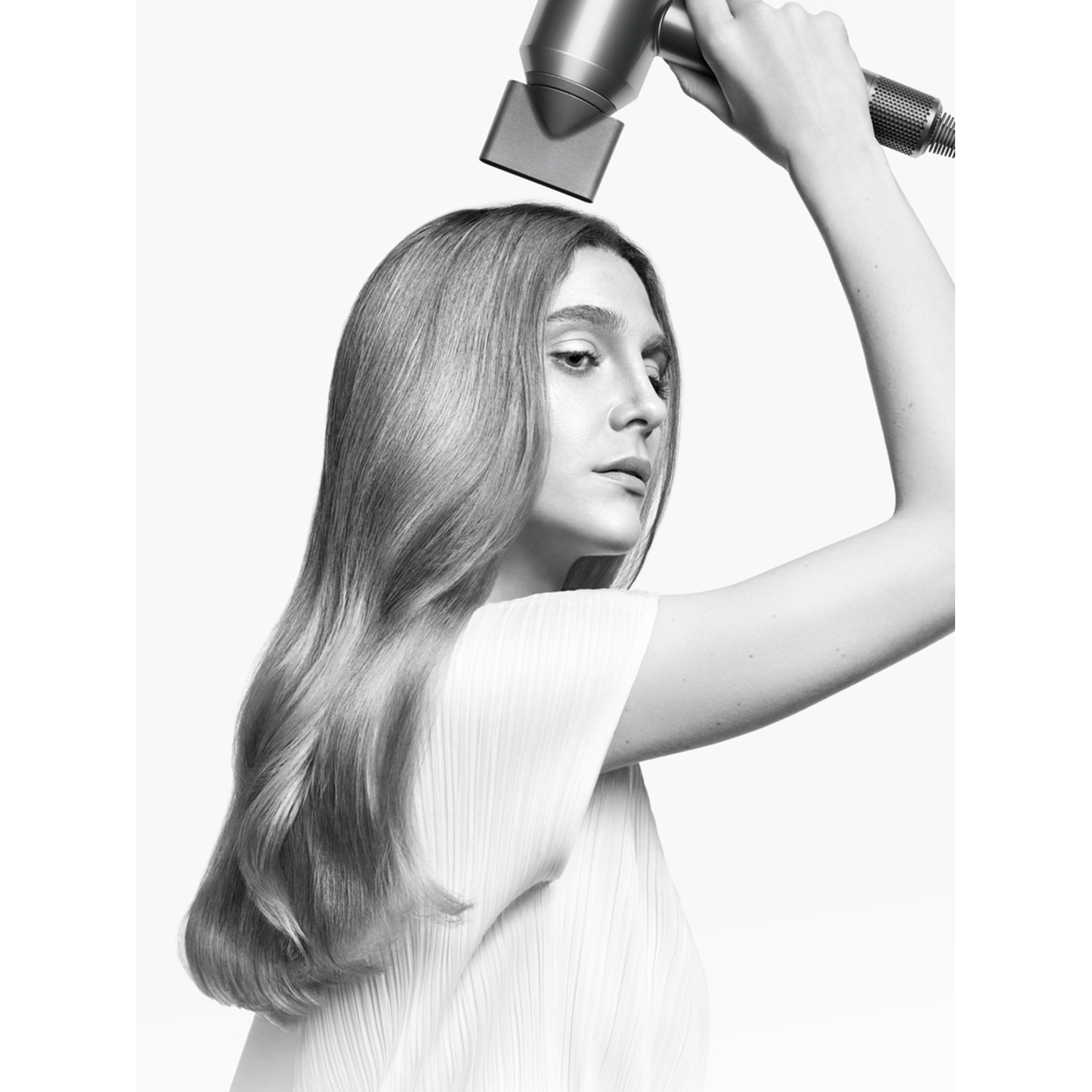 A woman uses a silver hairdryer to dry her long blonde hair.