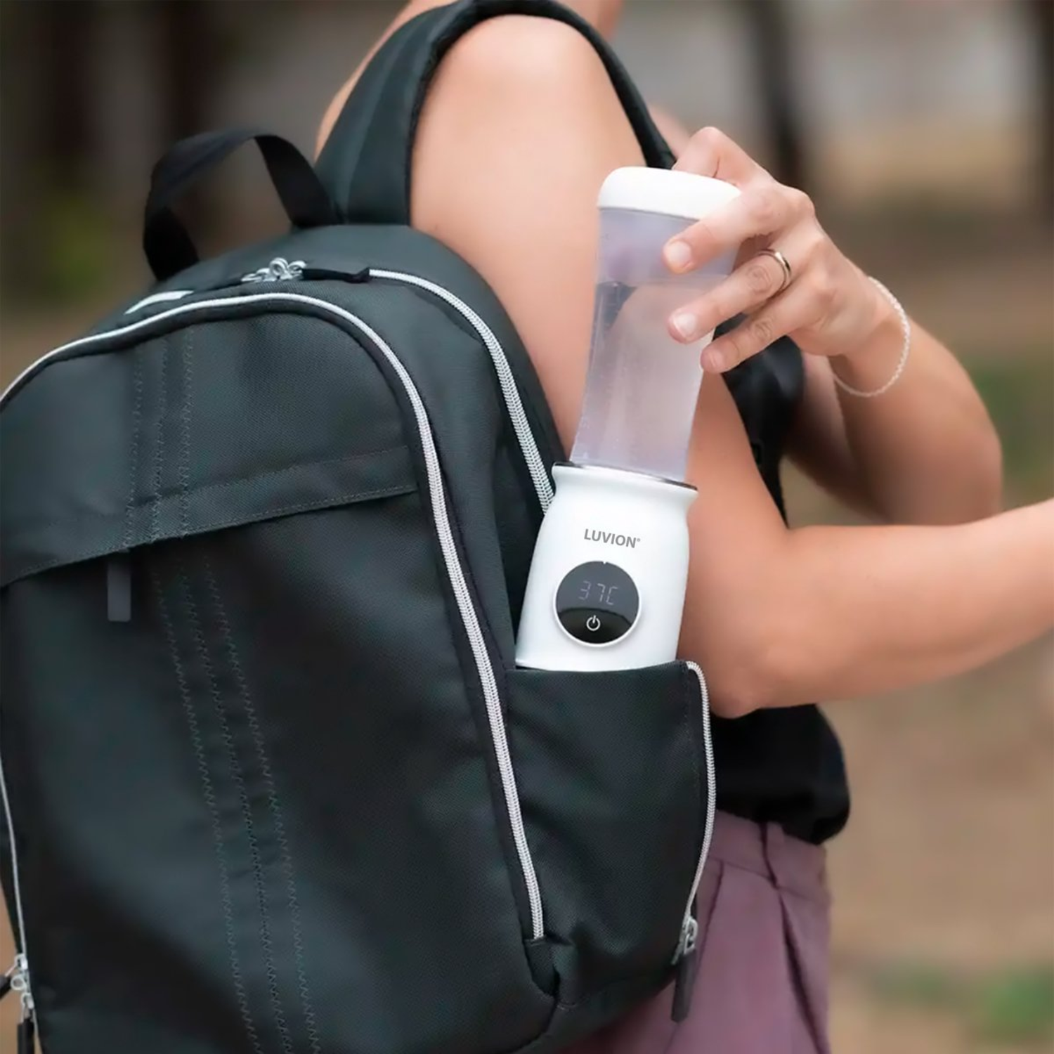 A person holding a white baby bottle warmer in a backpack's side pocket.