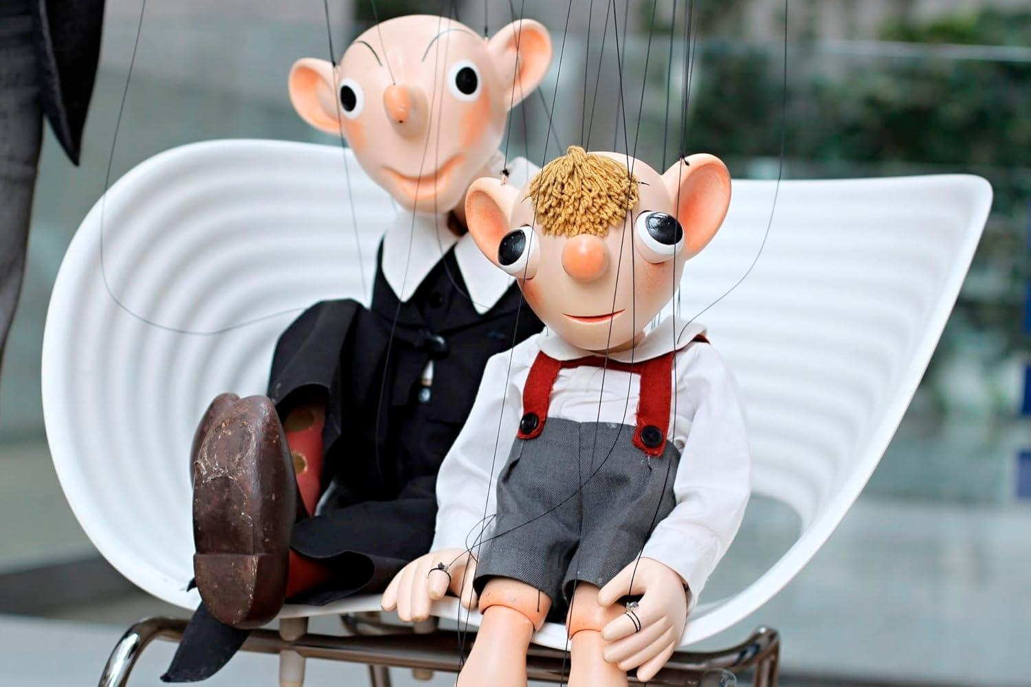 Zwei Marionettenpuppen sitzen auf einem weißen Stuhl, mit detaillierten Gesichtern und Kleidung.