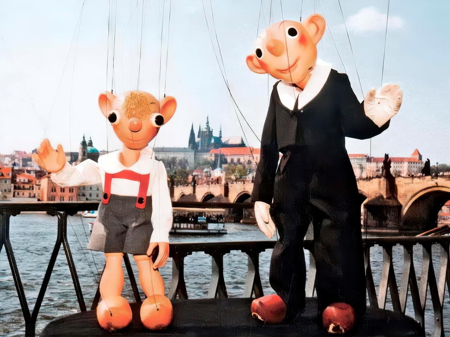 Zwei Marionetten auf einer Brücke, mit Stadt im Hintergrund.