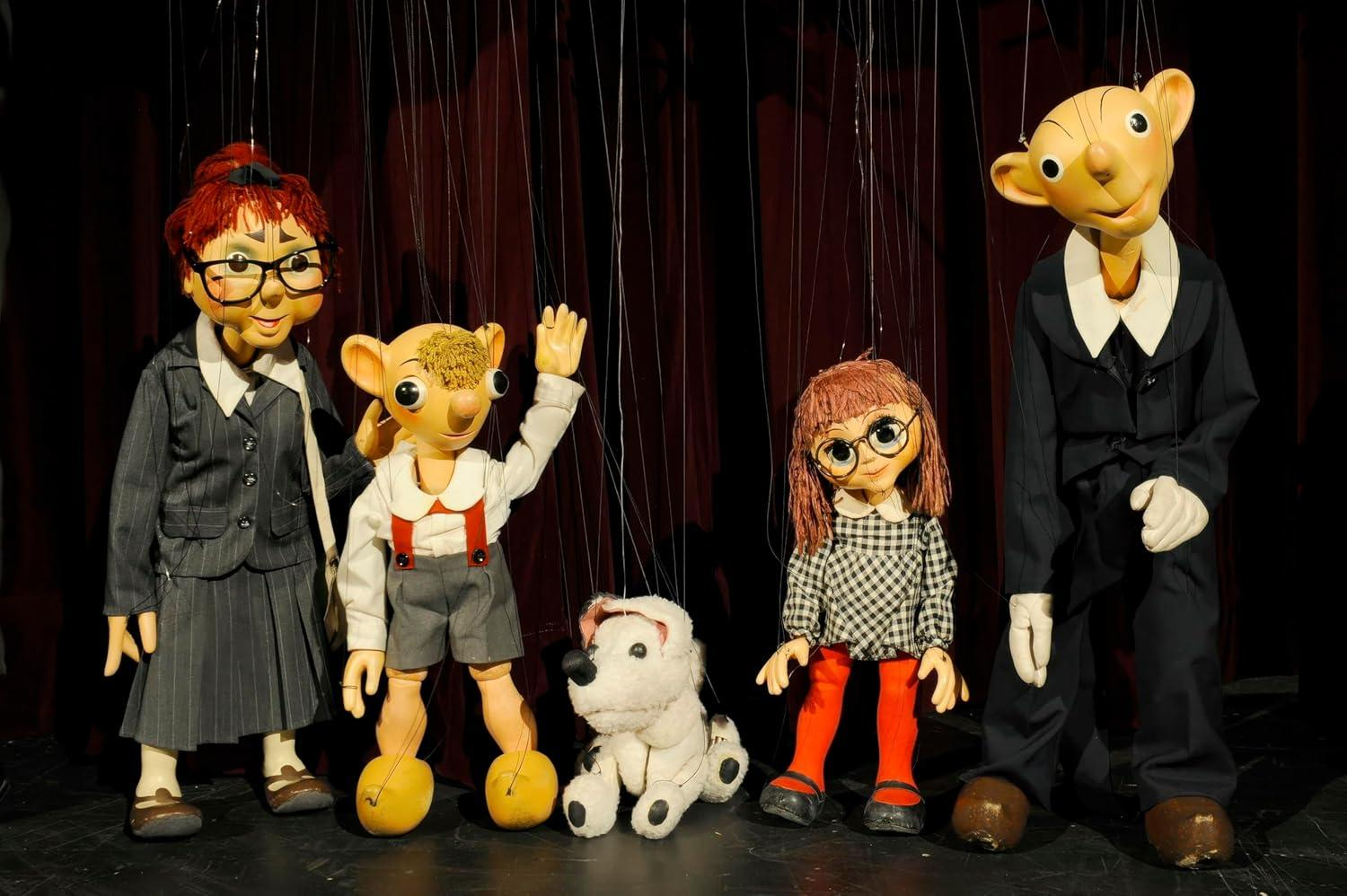 Fünf Puppen mit Brillen, in Anzügen und Kleidern, vor dunklem Hintergrund stehend.