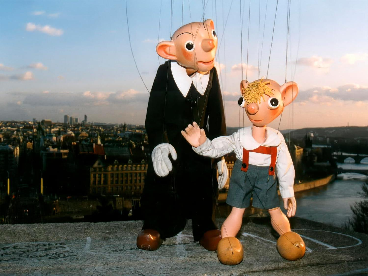 Zwei Marionettenpuppen mit Stadtkulisse; eine in Schwarz, eine in Grau.