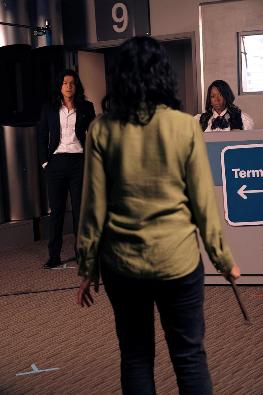 Eine Person im Vordergrund, zwei Personen im Hintergrund an einem Terminal, mit einem Schild.