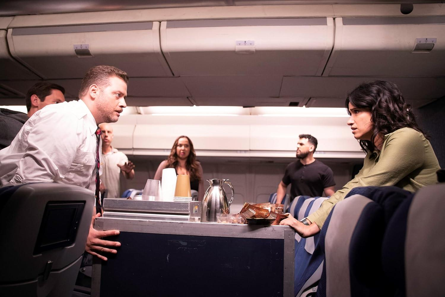 Passagiere in einer Flugzeugkabine, einige besorgt, mit einem Essenswagen in der Mitte.