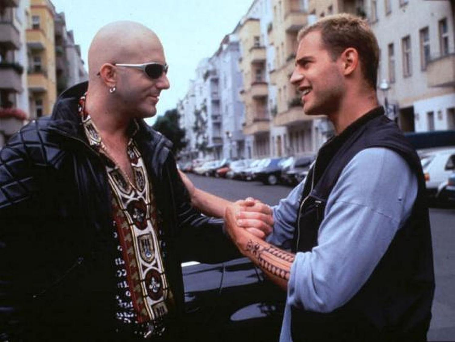 Zwei Männer geben sich auf der Straße die Hand, einer mit Glatze und Sonnenbrille.
