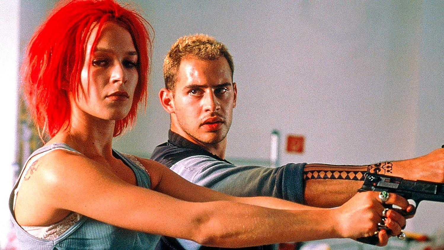 Ein Mann und eine Frau, die mit Waffen auf die Kamera zielen, mit Tattoos und rotem Haar.