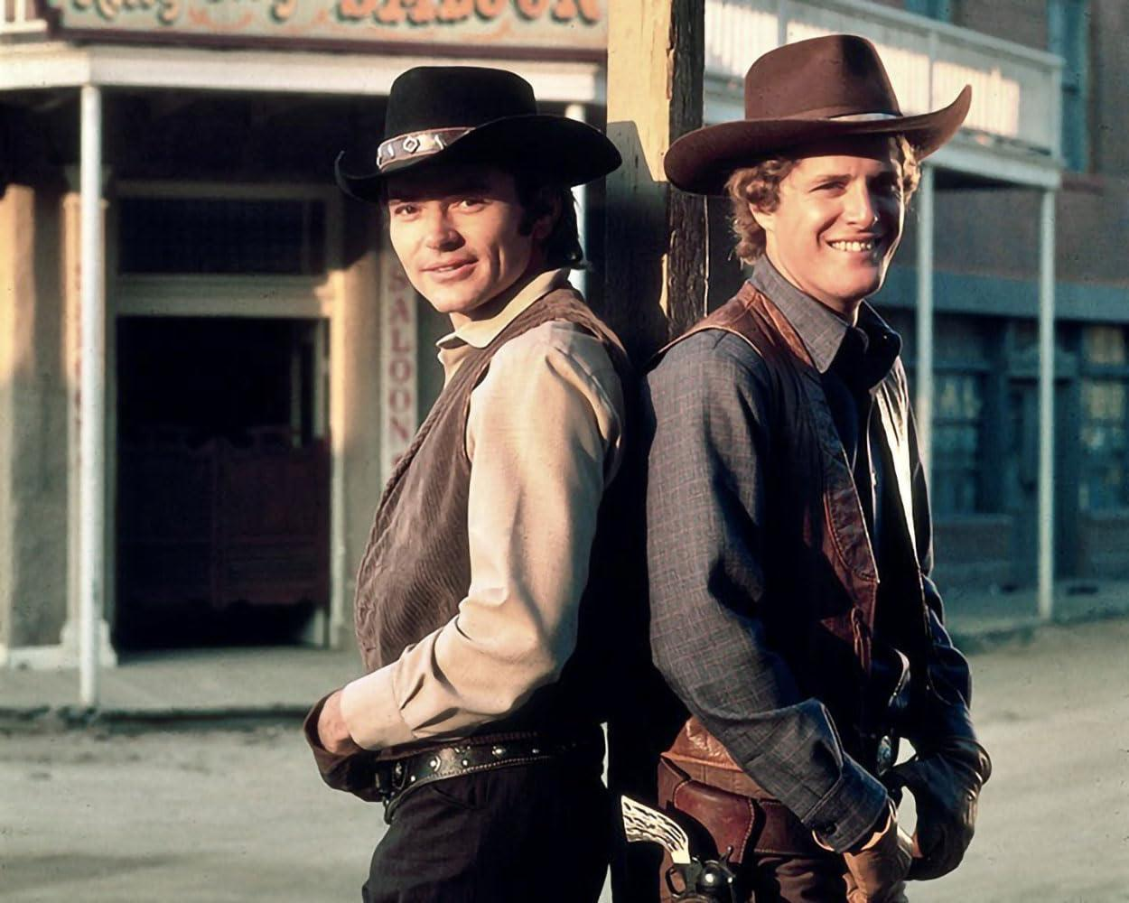 Zwei Männer mit Cowboyhüten lehnen sich Rücken an Rücken an ein Gebäude. Westernszene.