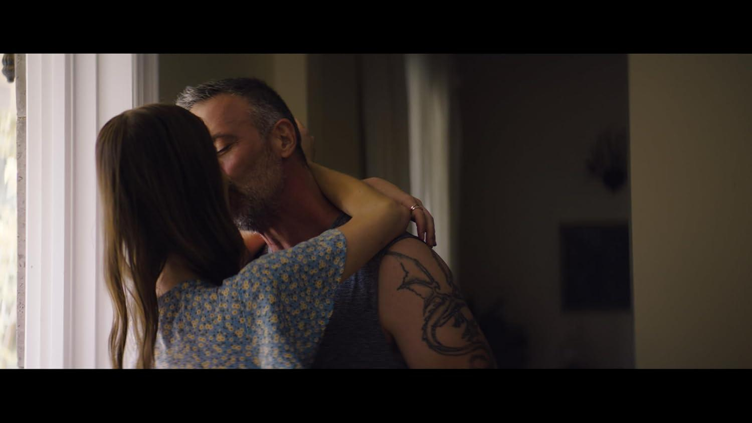 Ein küssendes Paar. Der Mann hat ein Tattoo und trägt ein Tanktop. Die Frau trägt ein Kleid.