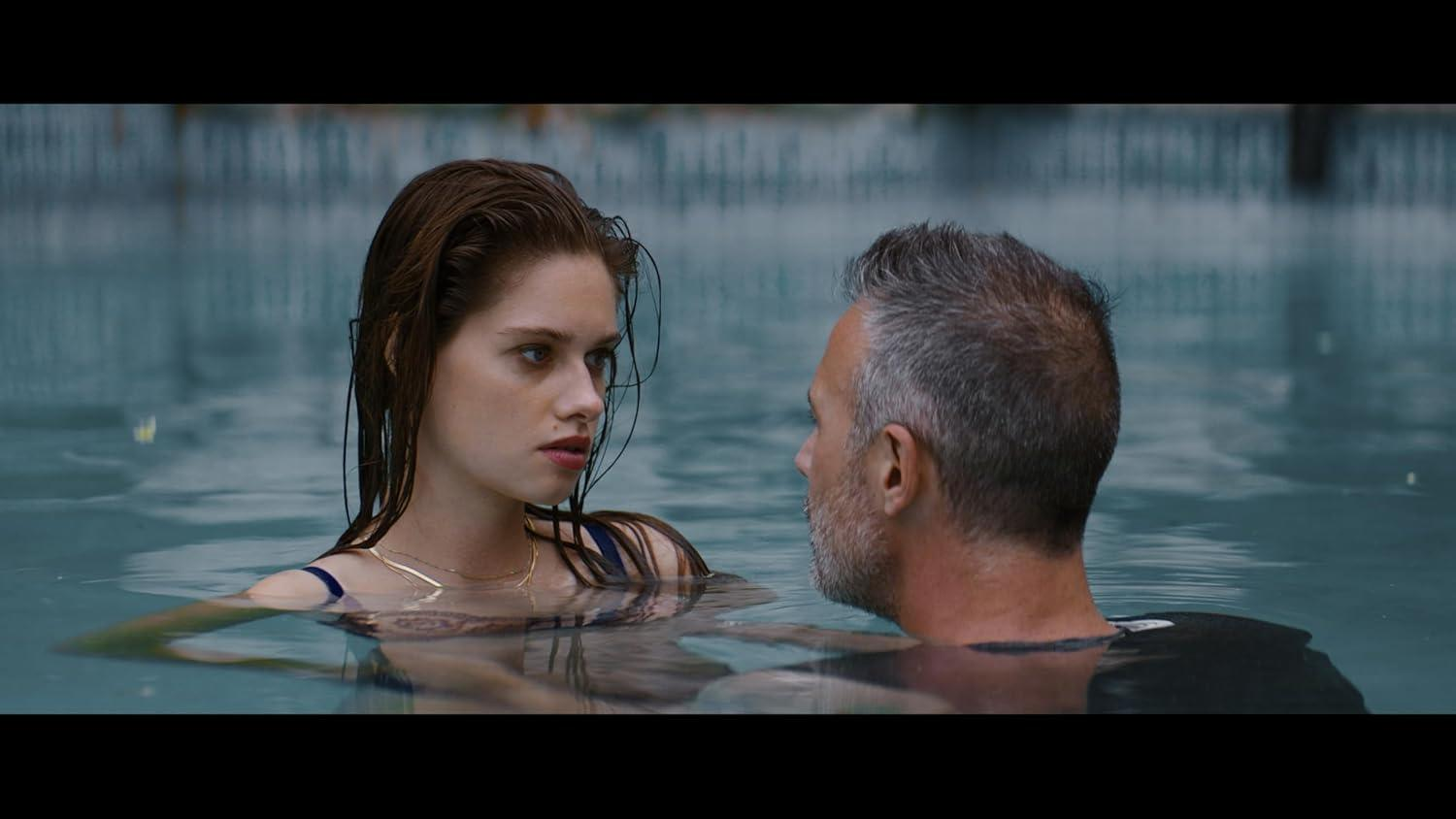 Eine Frau und ein Mann in einem Schwimmbad, die sich ansehen. Szene aus einem Film.