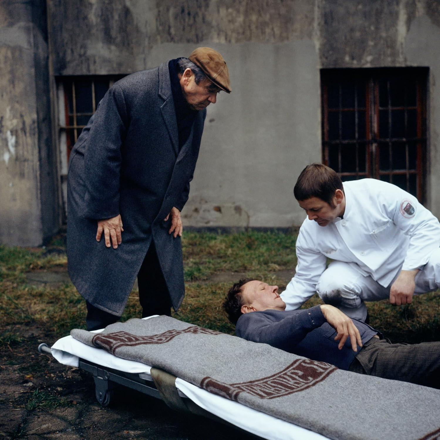 Eine Filmszene mit Männern um eine Person, die auf einer Bahre liegt.