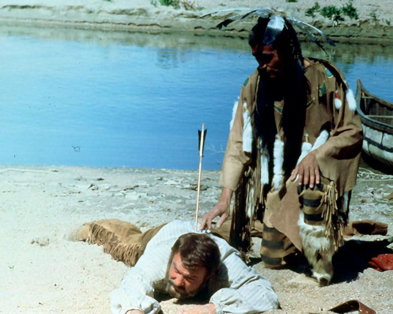 Indianer kniet über einem Mann mit Pfeil im Rücken am Strand.