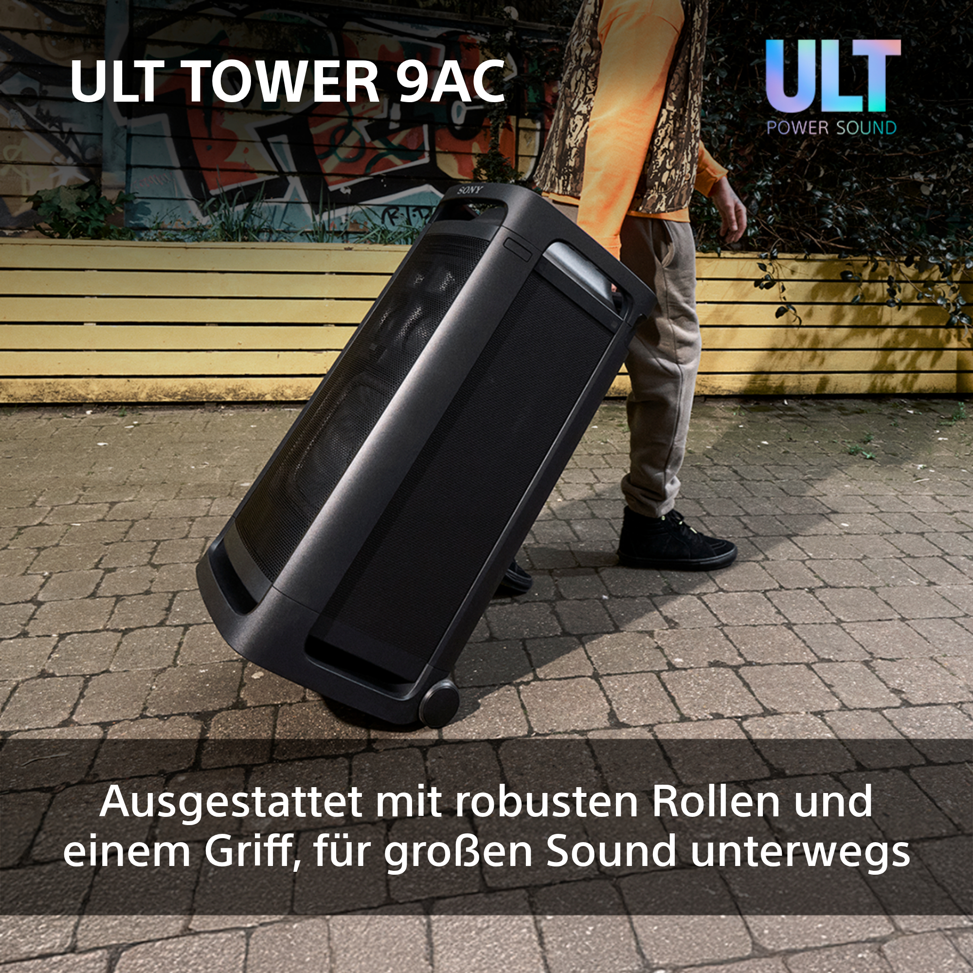 Eine schwarze Lautsprecherbox auf Rädern wird von einer Person geschoben. Auf dem Lautsprecher steht ULT Tower 9AC.