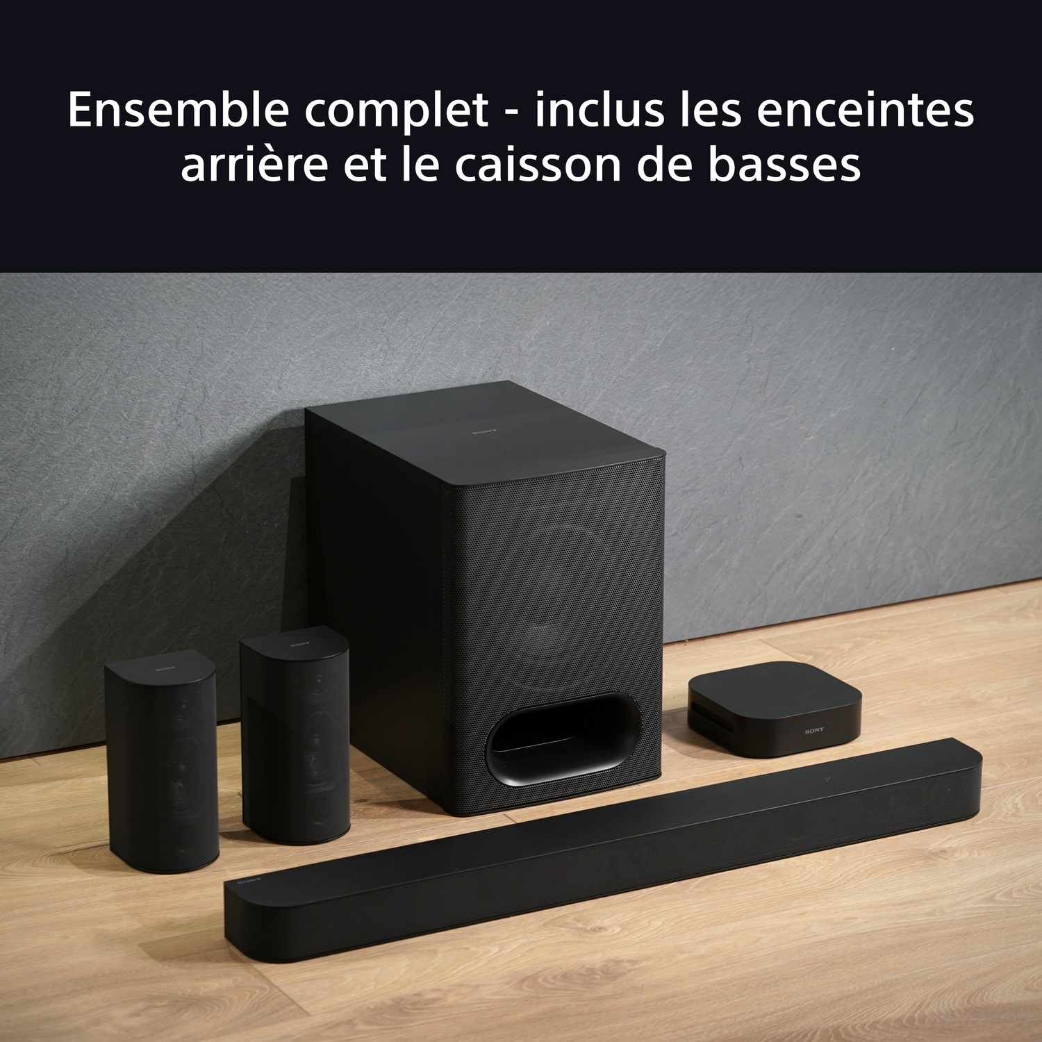 Système home cinéma noir avec barre de son, deux enceintes et un caisson de basses sur plancher bois.