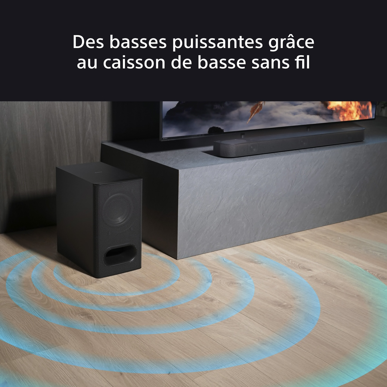 Caisson de basses noir avec ondes sonores sans fil sur un sol en bois, à côté d'une TV et d'une barre de son.