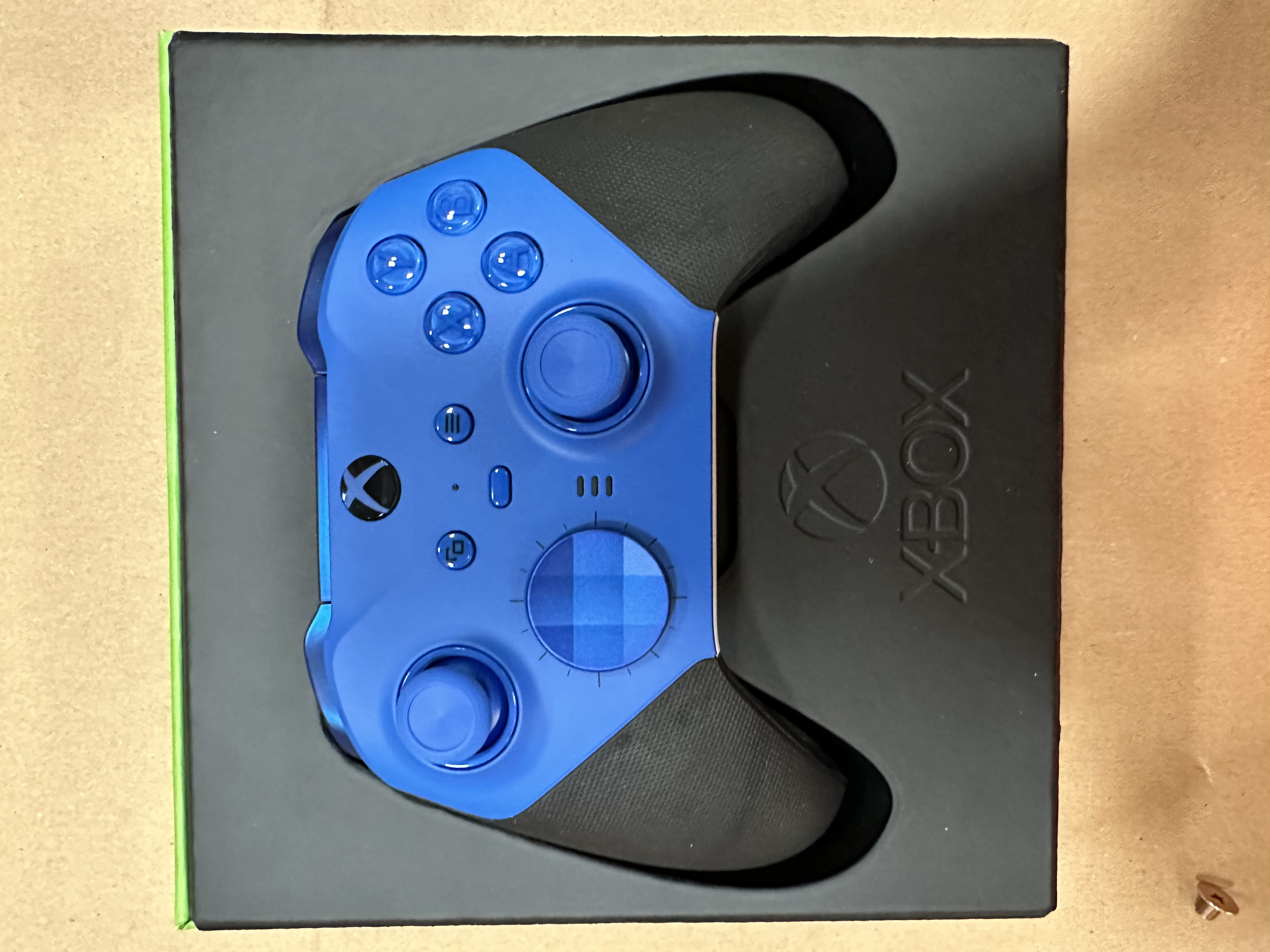 Niebiesko-czarny kontroler Xbox jest pokazany w czarnym pudełku z zieloną obwódką.