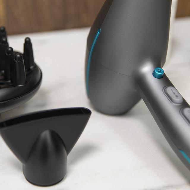 Szara suszarka do włosów z czarnymi nasadkami na białej powierzchni.