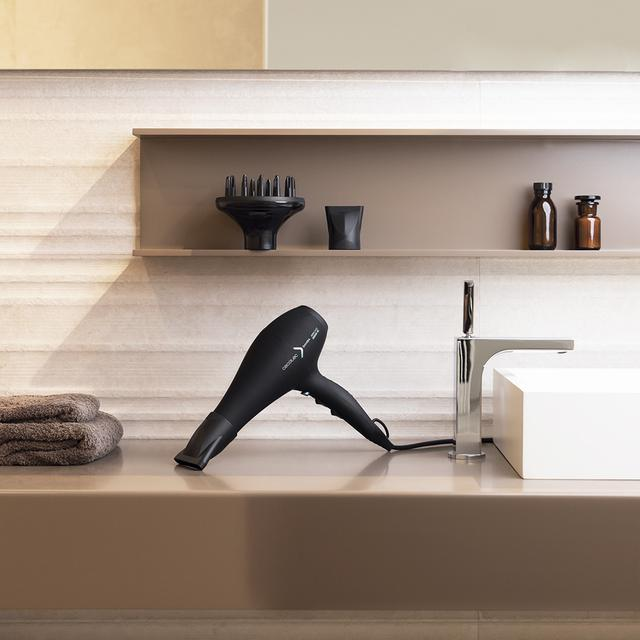 Czarna suszarka do włosów na blacie, obok lustra i innych akcesoriów łazienkowych.