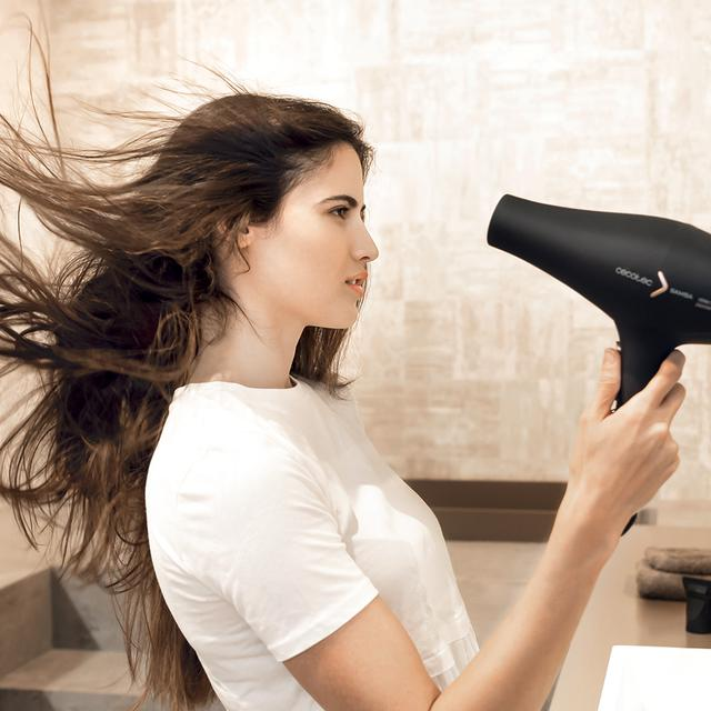 Kobieta używająca suszarki do włosów, jej włosy odchylają się w łazience.