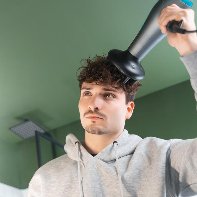 Mężczyzna używa suszarki do włosów na głowie.