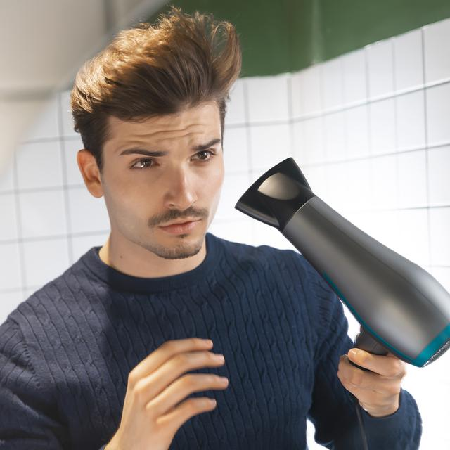 Mężczyzna patrzący w lustro trzymający czarno-szarą suszarkę do włosów.