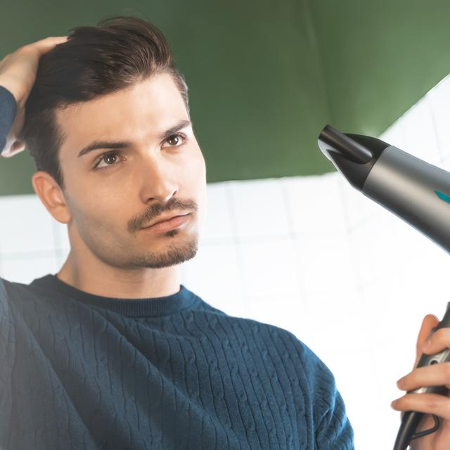 Mężczyzna patrzy na włosy z suszarką do włosów.