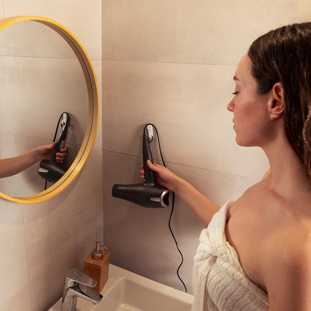 Kobieta w łazience suszy włosy czarną suszarką.