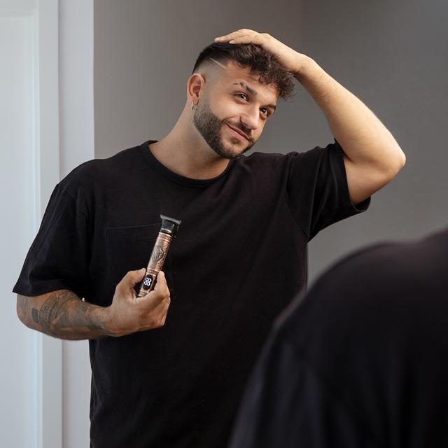 Mężczyzna patrzący w lustro, trzymający trymer do włosów, z przyciętą fryzurą.