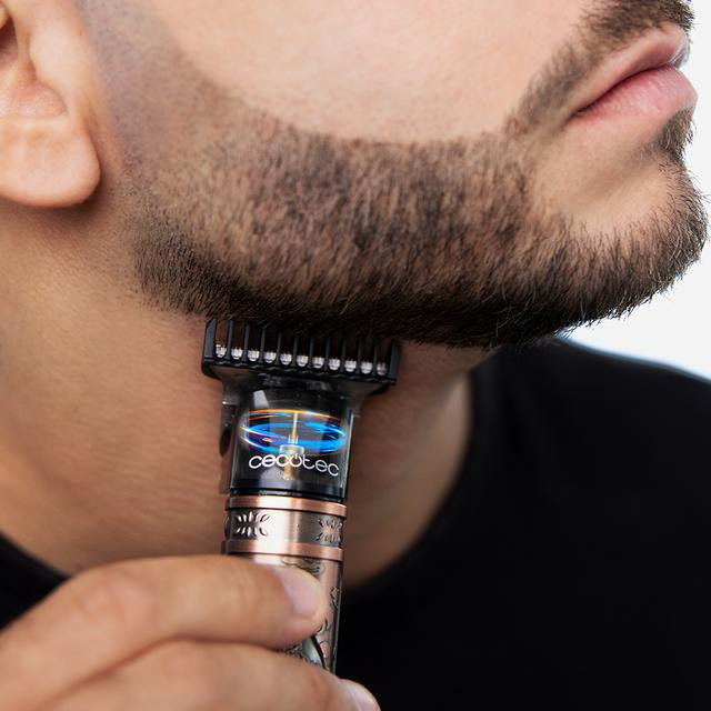 Mężczyzna przycina brodę czarno-srebrną elektryczną maszynką, ujęcie z bliska.