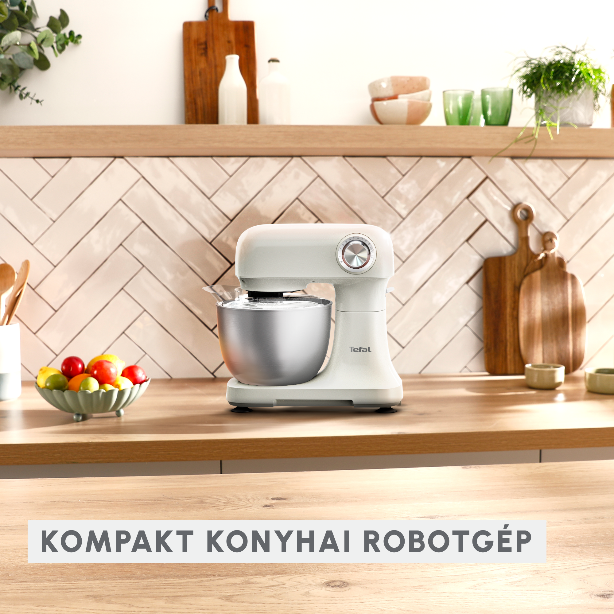 Fehér konyhai robotgép fa pulton, gyümölcsökkel és konyhai eszközökkel.