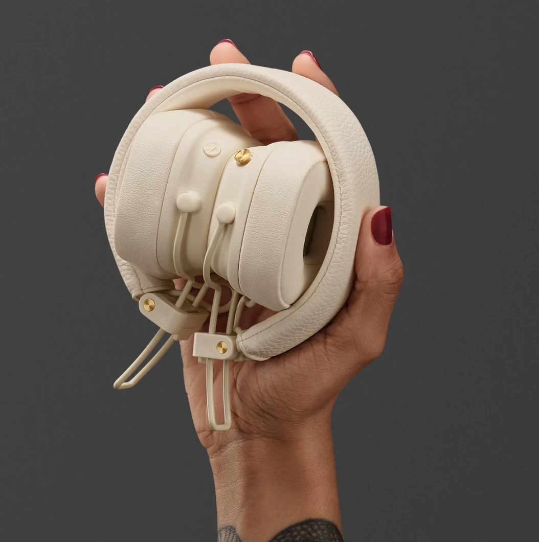 Złożone kremowe słuchawki w dłoni z czerwonym lakierem do paznokci.