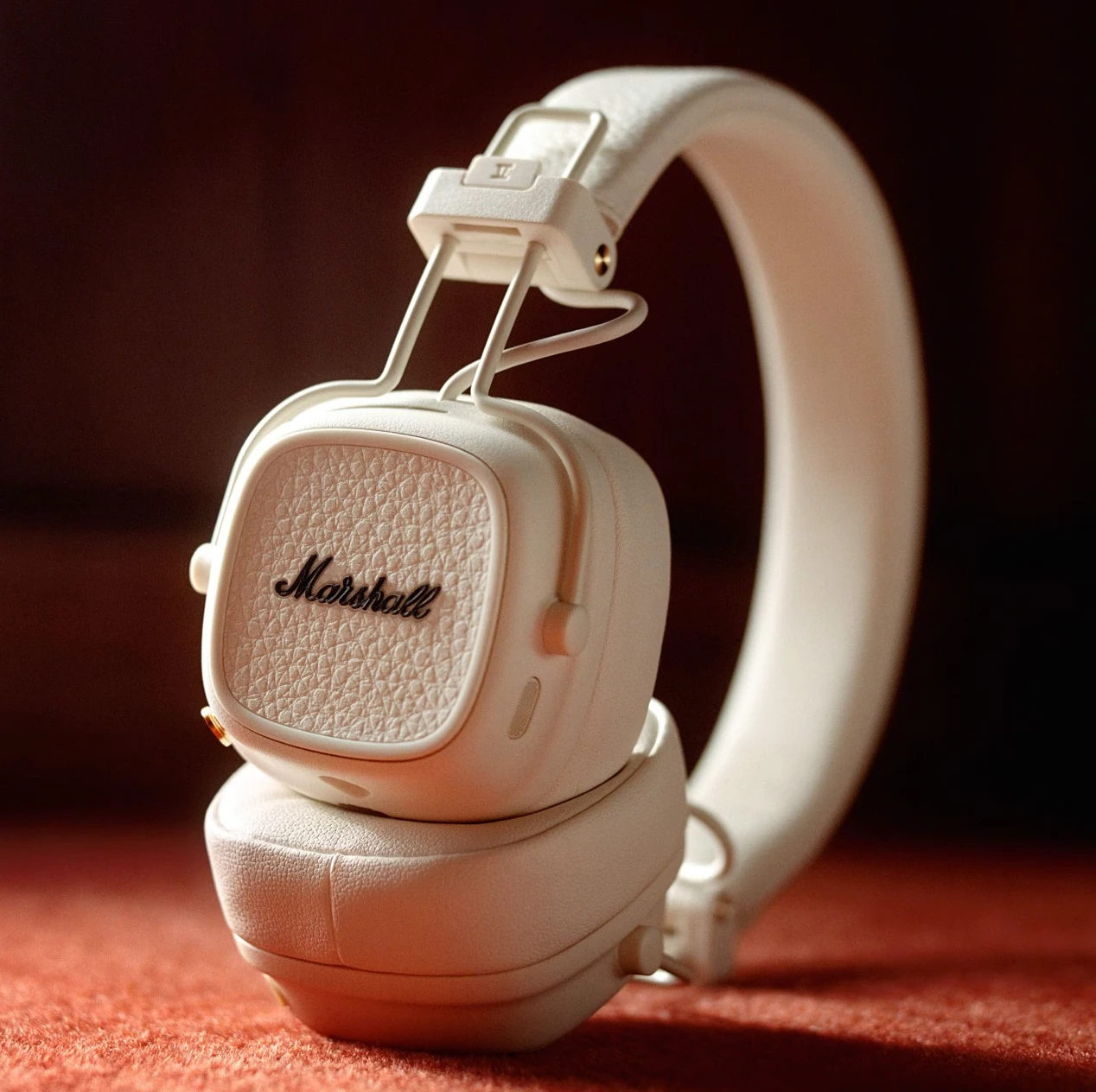 Białe słuchawki Marshall na czerwonej powierzchni.