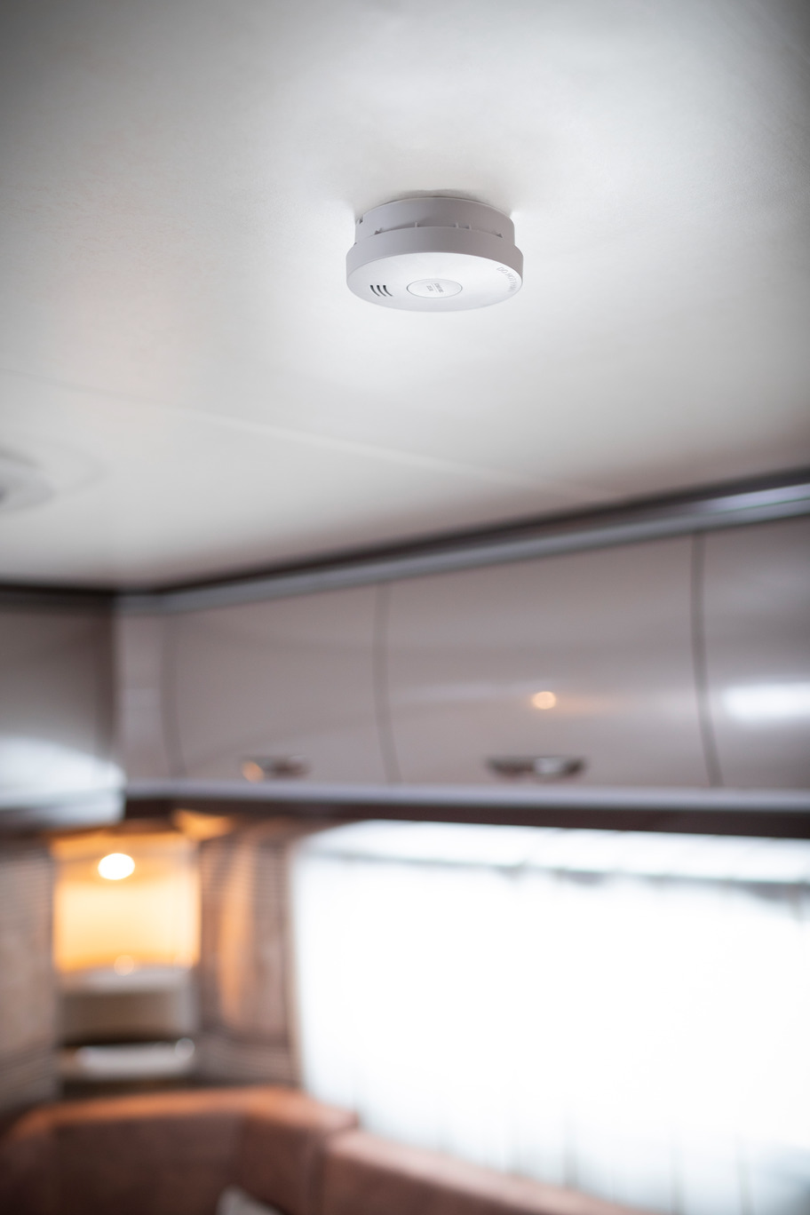 Czujnik dymu na białym suficie. Wnętrze domu. Delikatne oświetlenie.