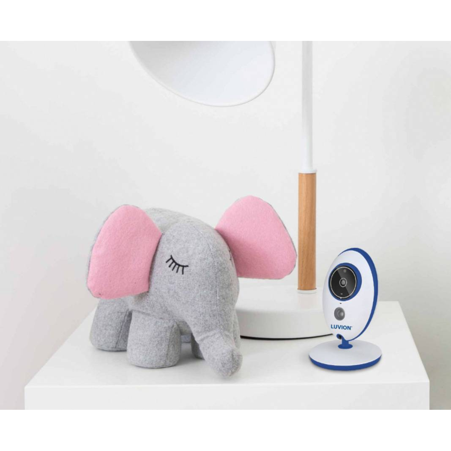 Grijs olifantenspeelgoed, witte lamp en babyfoon op een witte tafel.