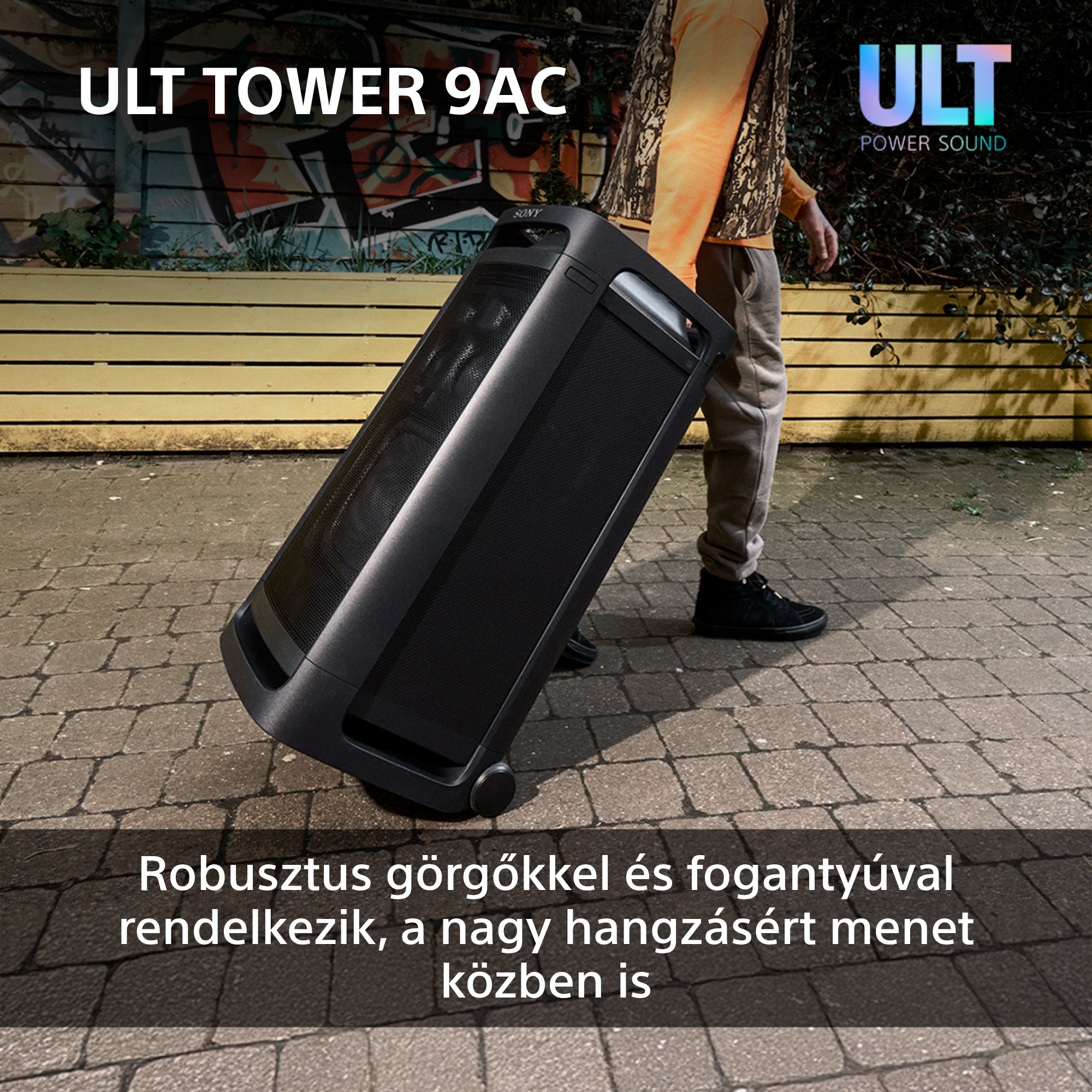 Személy fekete hangszórót húz kerekeken. Magyar nyelvű szöveg látható.