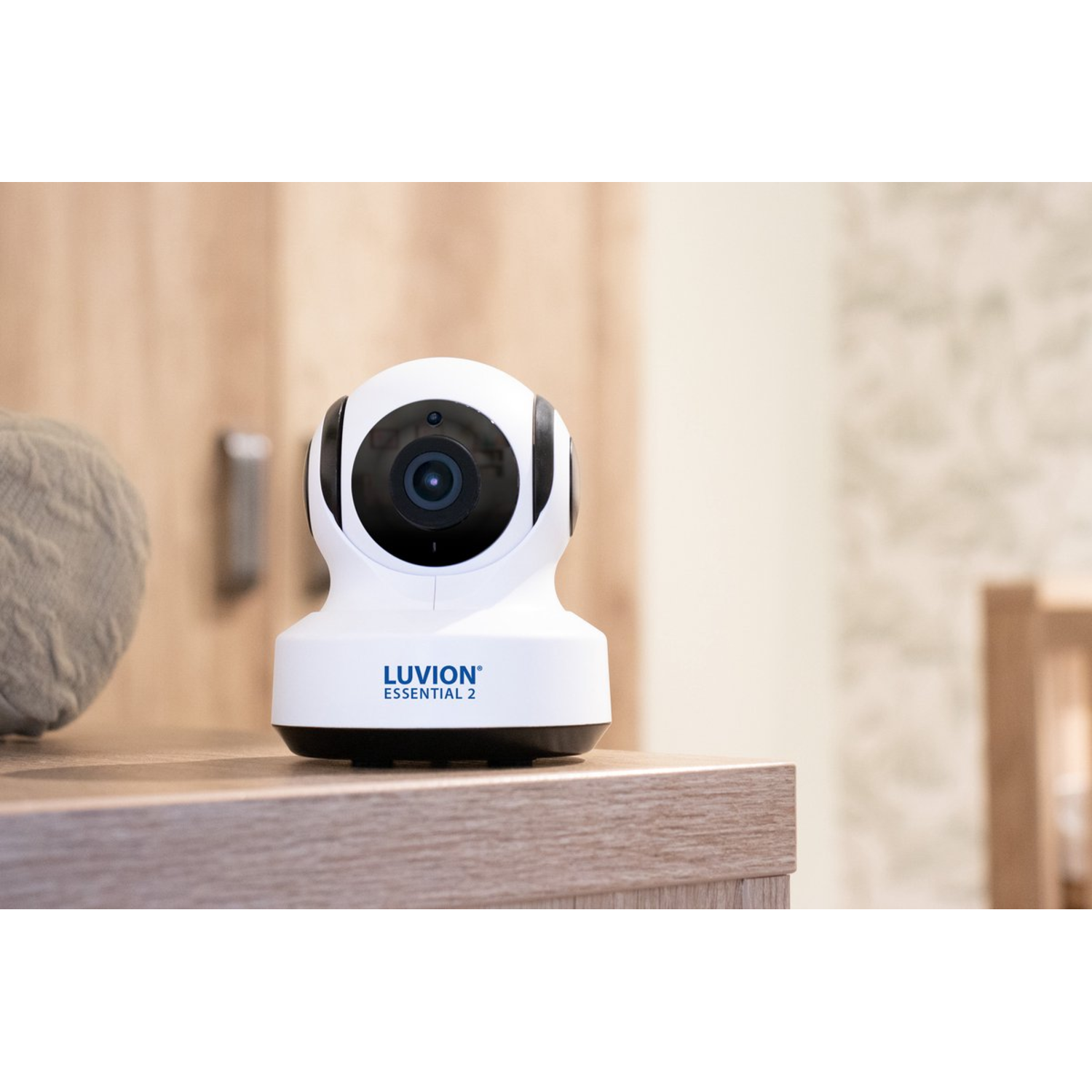 White baby monitor on a wood surface. It has a black lens and a blue text.
