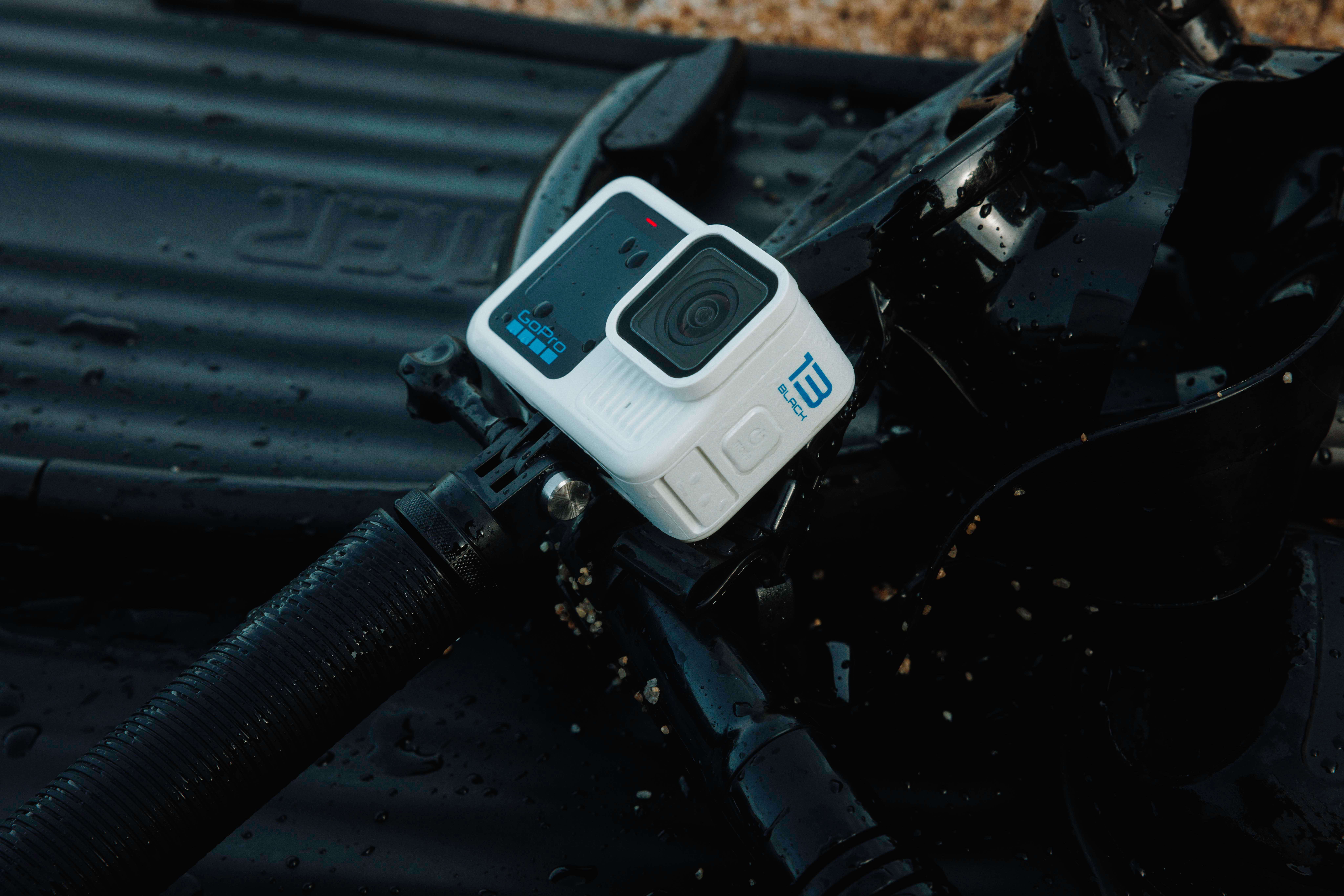 Weiße GoPro-Kamera mit schwarzen Details auf schwarzem Untergrund. Die Kamera liegt neben schwarzem Zubehör.