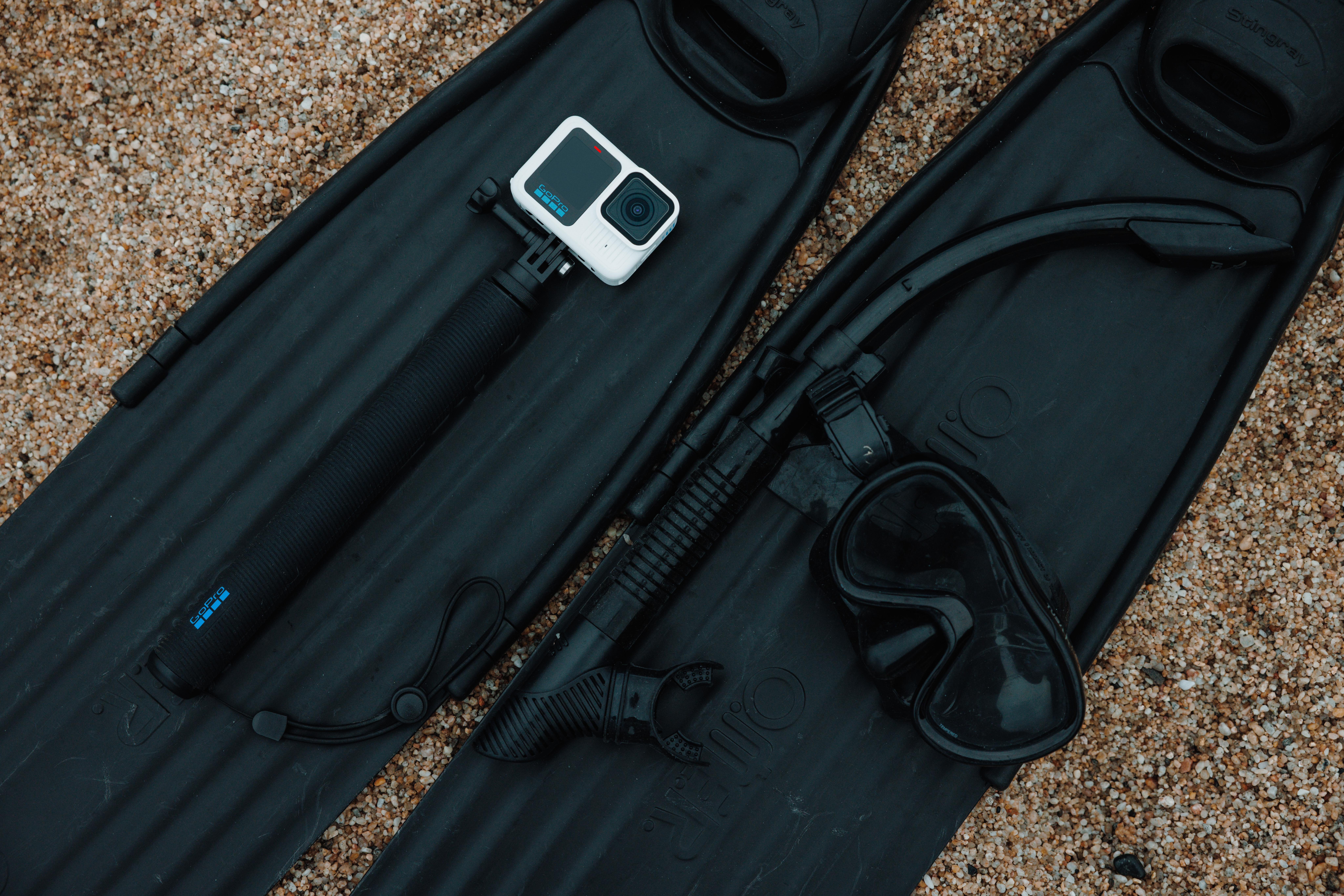 GoPro-Kamera auf einem Selfie-Stick, Schnorchel und Maske sowie Flossen auf Sand.