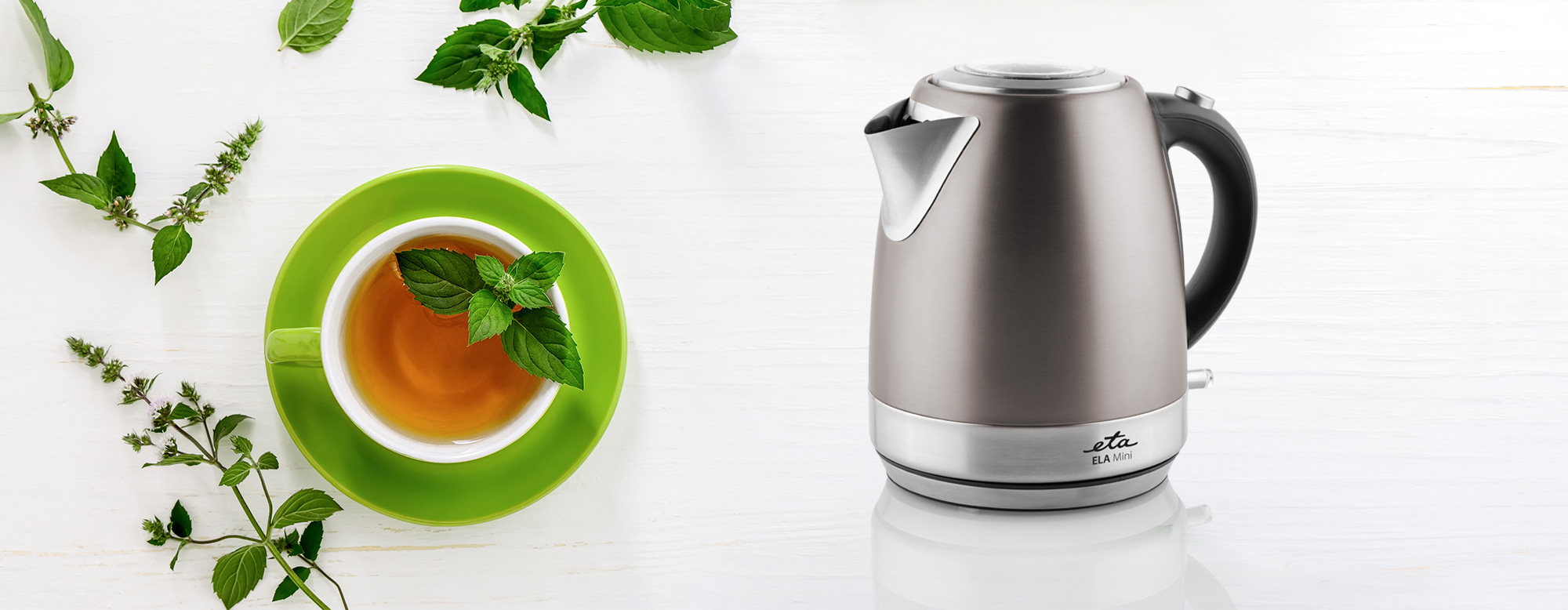 Egy vízforraló és egy csésze tea menta ággal, fehér felületen.
