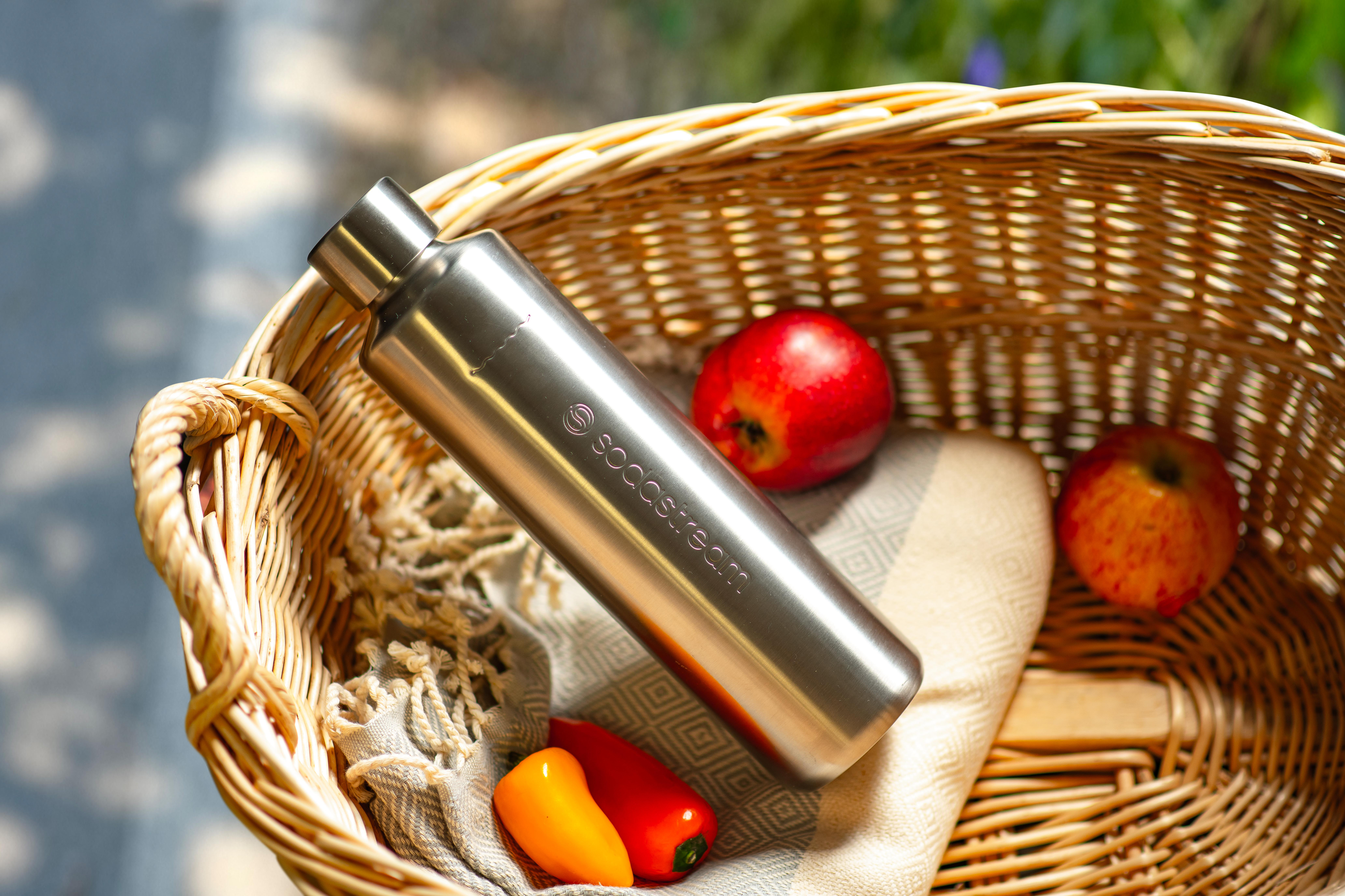 Edelstahl-Wasserflasche in einem Weidenkorb mit roten Äpfeln und Paprika.