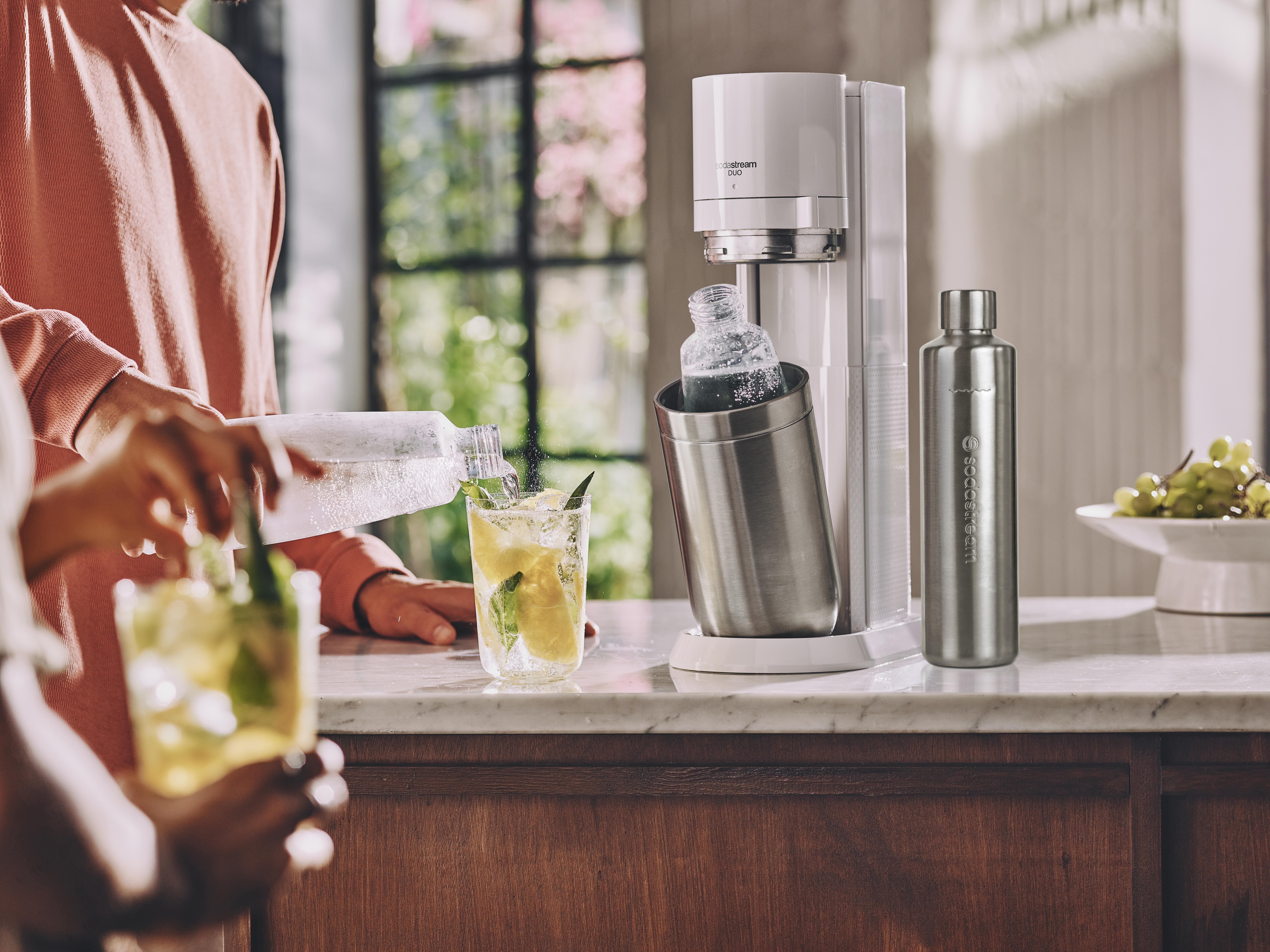 Leute machen Getränke. Soda-Maker und Wasserflasche auf der Theke. Glas mit Getränk.