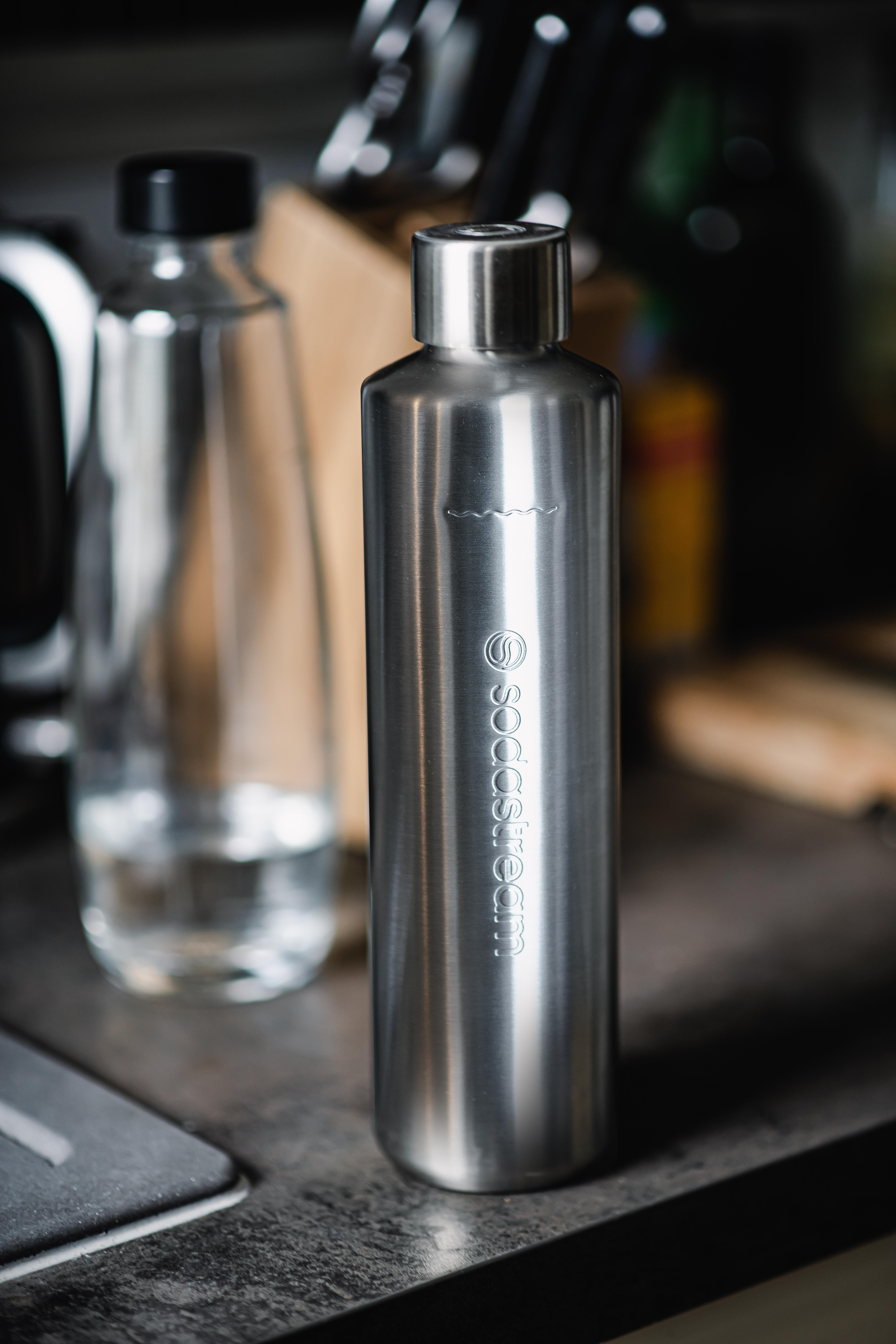 Eine Edelstahl-Wasserflasche mit SodaStream-Logo, neben einer Glasflasche mit Wasser.
