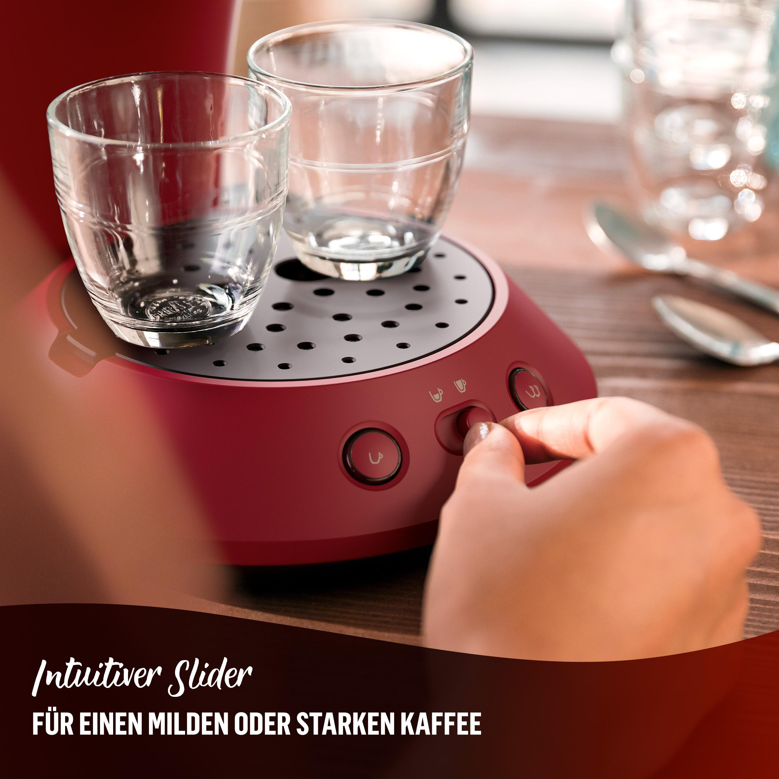 Eine rote Kaffeemaschine mit zwei Gläsern und einer Hand, die einen Knopf drückt.