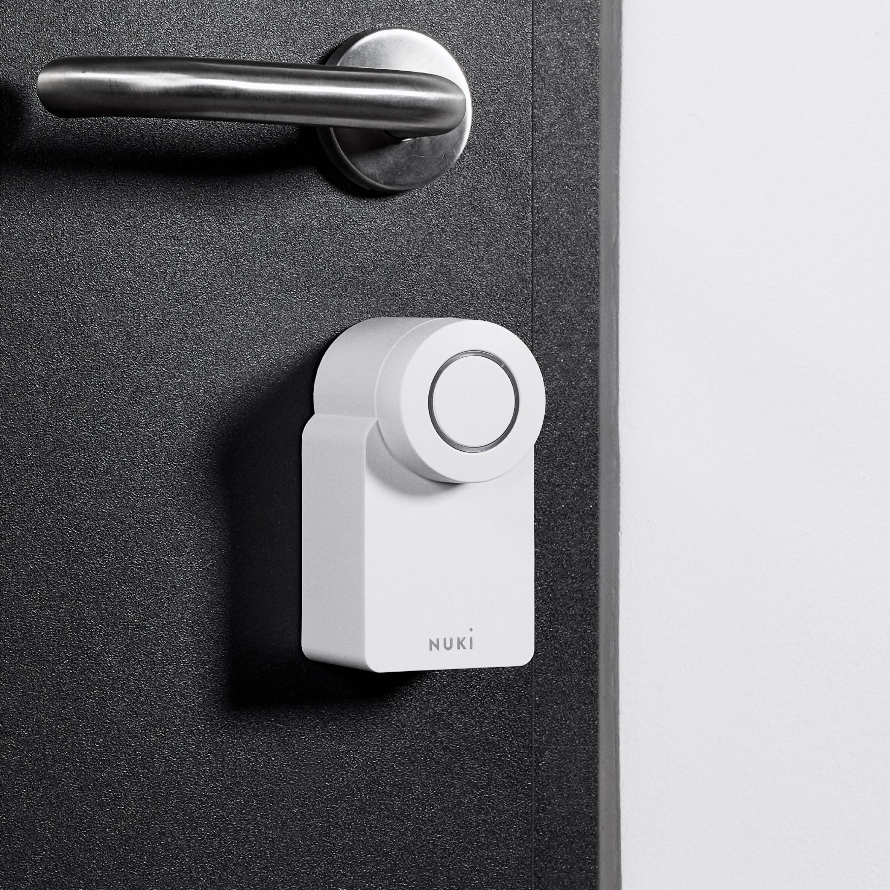 Weißes Smart Lock an einer schwarzen Tür befestigt, mit dem Nuki-Logo sichtbar.