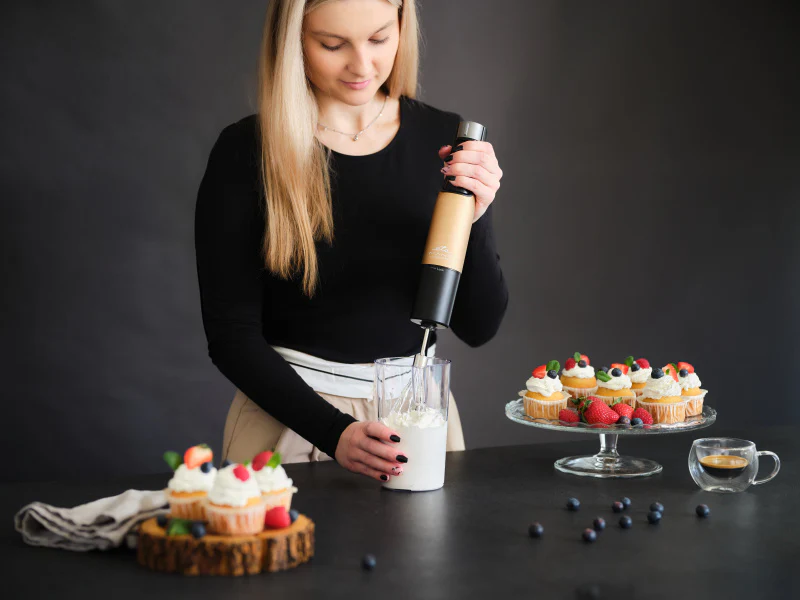 Egy nő kézi mixerrel habot ver, közeli cupcake-ekkel.