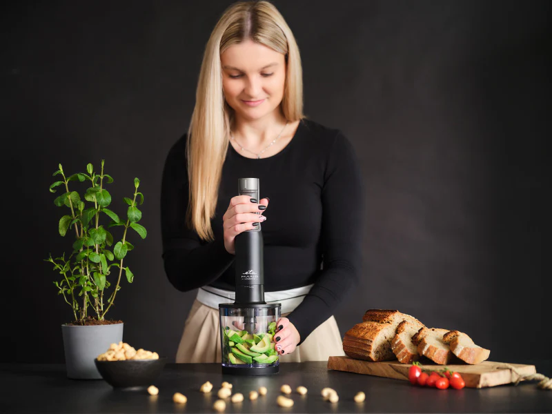 Szöszi nő fekete botmixert használ avokádó keveréséhez átlátszó edényben.