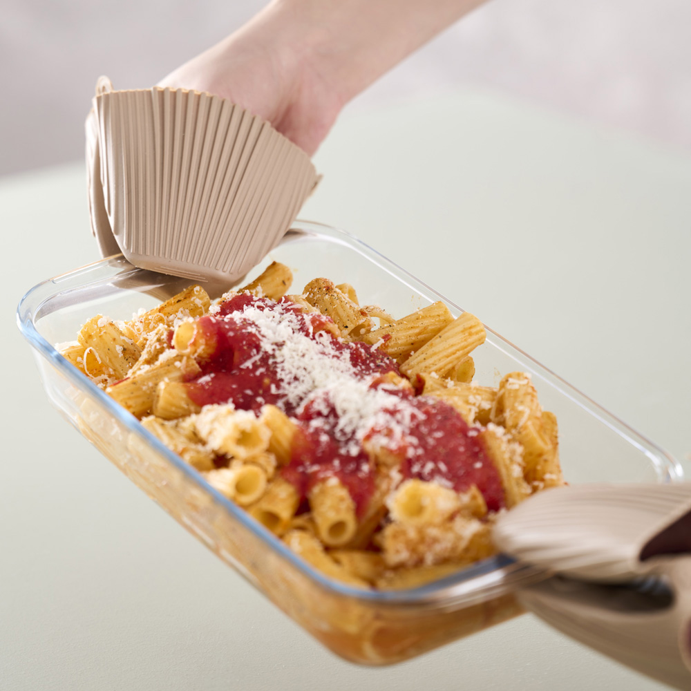 Persona sosteniendo pasta horneada en un plato de vidrio con guantes de cocina.