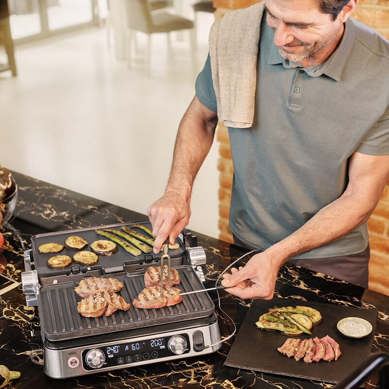 Férfi grillez ételt grillen, zöldségekkel és hússal az asztalon.
