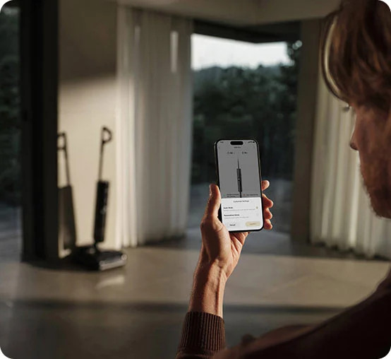 Mężczyzna trzyma telefon z aplikacją do odkurzacza, w tle dwa odkurzacze.