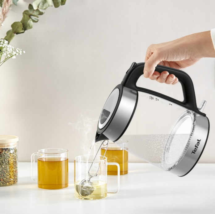 Osoba nalewa wodę z przezroczystego czajnika do dwóch szklanek z zaparzaczami do herbaty.